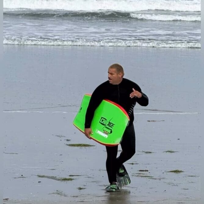 Wetsuit-clad person carrying neon green bodyboard
